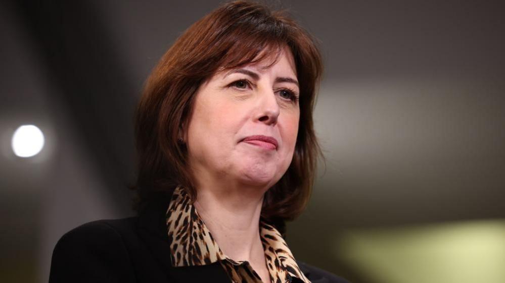 Close-up of Lucy Powell as she looks off to the right. She is wearing a leopard print blouse and black suit jacket