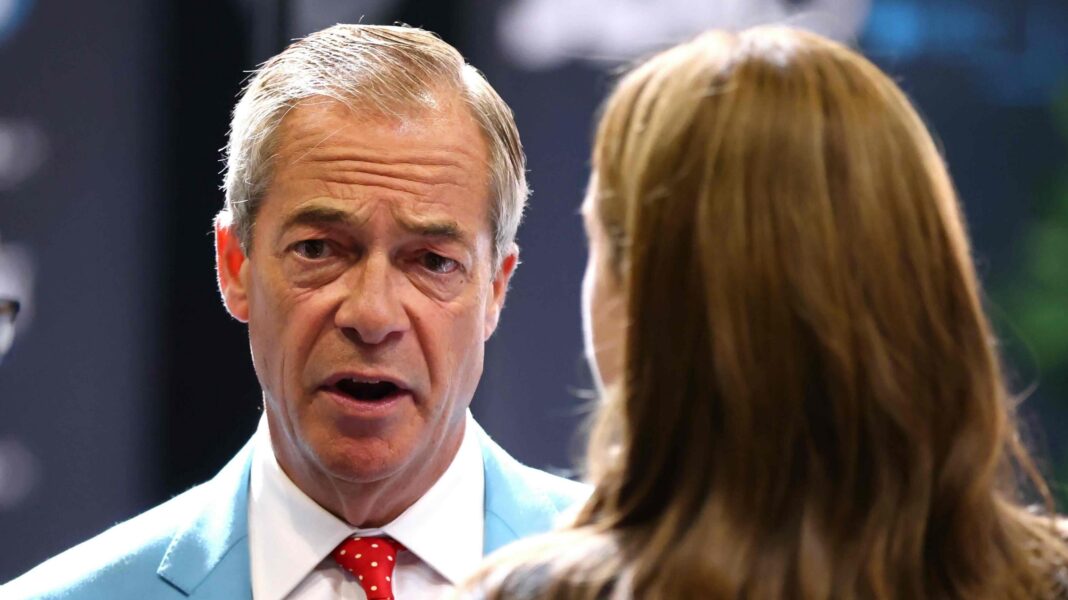Farage, seen from the shoulders up and wearing a light blue suit and red polka dot tie, talks to a woman with long brown hair who is seen from behind.