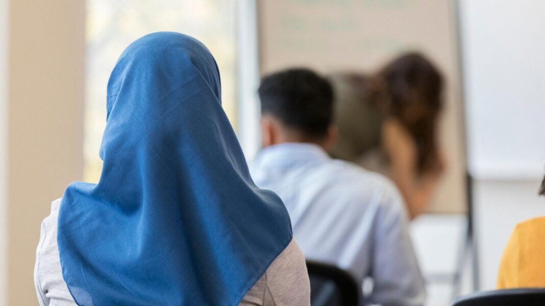 Austria’s Islamic headscarf ban in force as under-14s go back to school A stock image of a girl wearing a blue headscarf. She is sitting down in a classroom, facing with her back towards the camera.