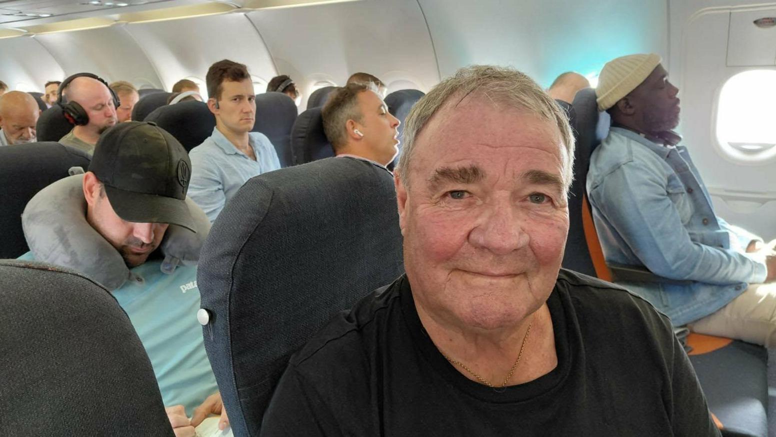 Phil White smiles at the camera as he sits on an EasyJet plane