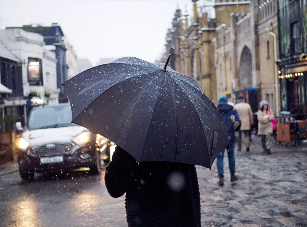 A person holding a black umbrella stands in the rain