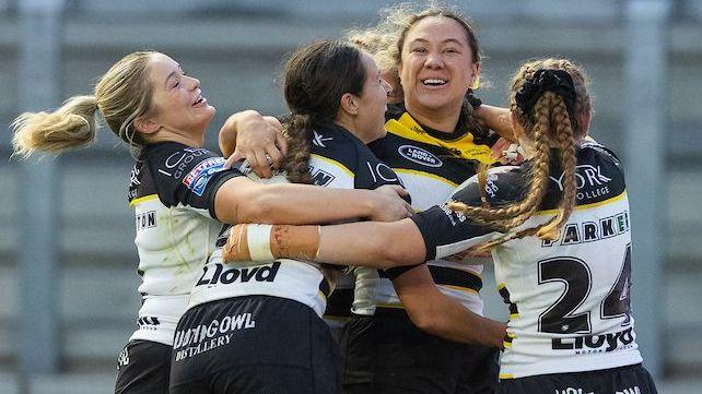 York Valkyrie forward Adaoha Akwiwu smiles broadly as she is mobbed by team-mates, all in white and back, after scoring a try against Leeds Rhinos.
