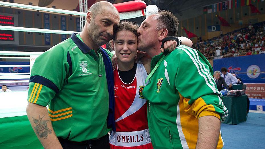Katie Taylor is hugged by her dad and her coach
