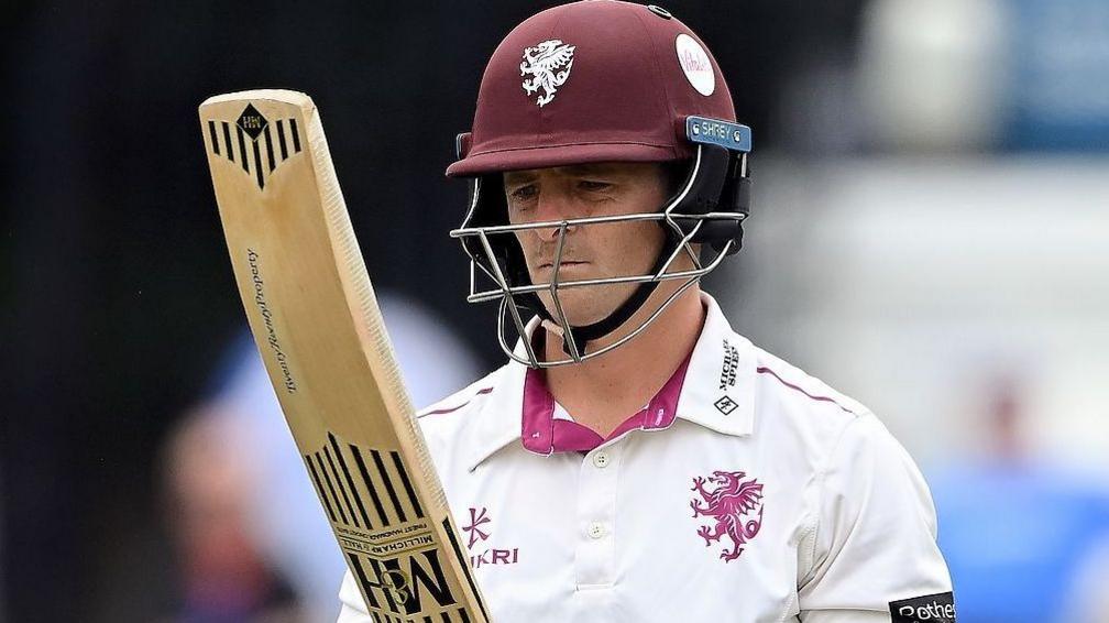 Tom Abell, wearing a white shirt and claret helmet, looks at his bat