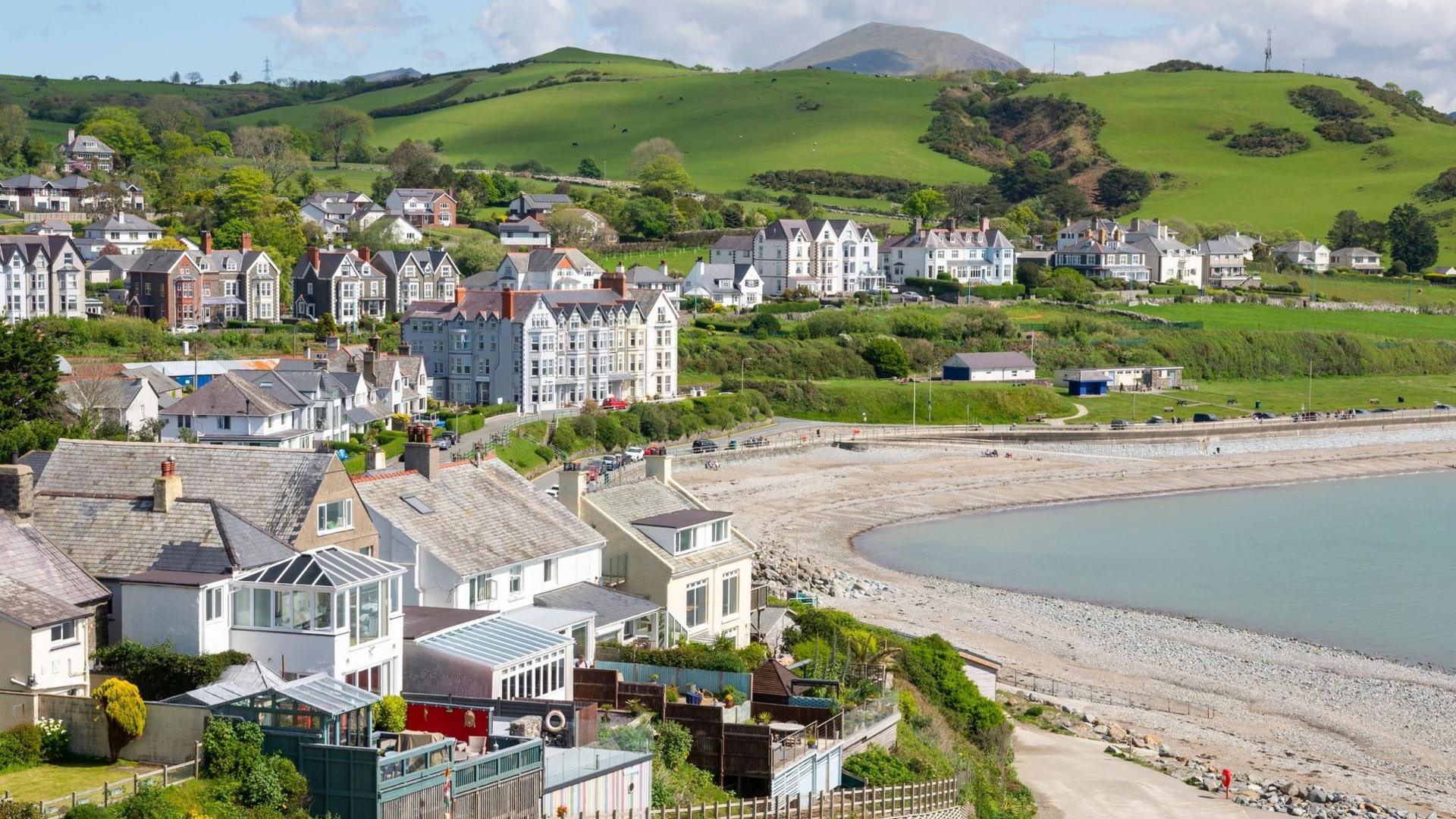 General view of the seaside town of Criccieth in north Wales, including a pebble beach and large townhouses overlooking the seafront, in the sunshine.