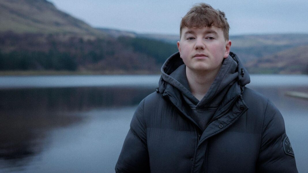 Boy abducted by mum has renewed ‘sense of purpose’ Alex Batty, who is wearing a black coat and hooded top, is standing in front of a large lake.