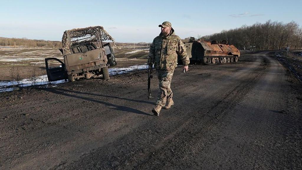 A fighter of the Chechen Akhmat battalion walks near destroyed military vehicles on a road near the village of Kazachya Loknya, which was previously held by Ukrainian troops and recently retaken by Russia's armed forces, in the Sudzha district of the Kursk region on March 18, 2025,