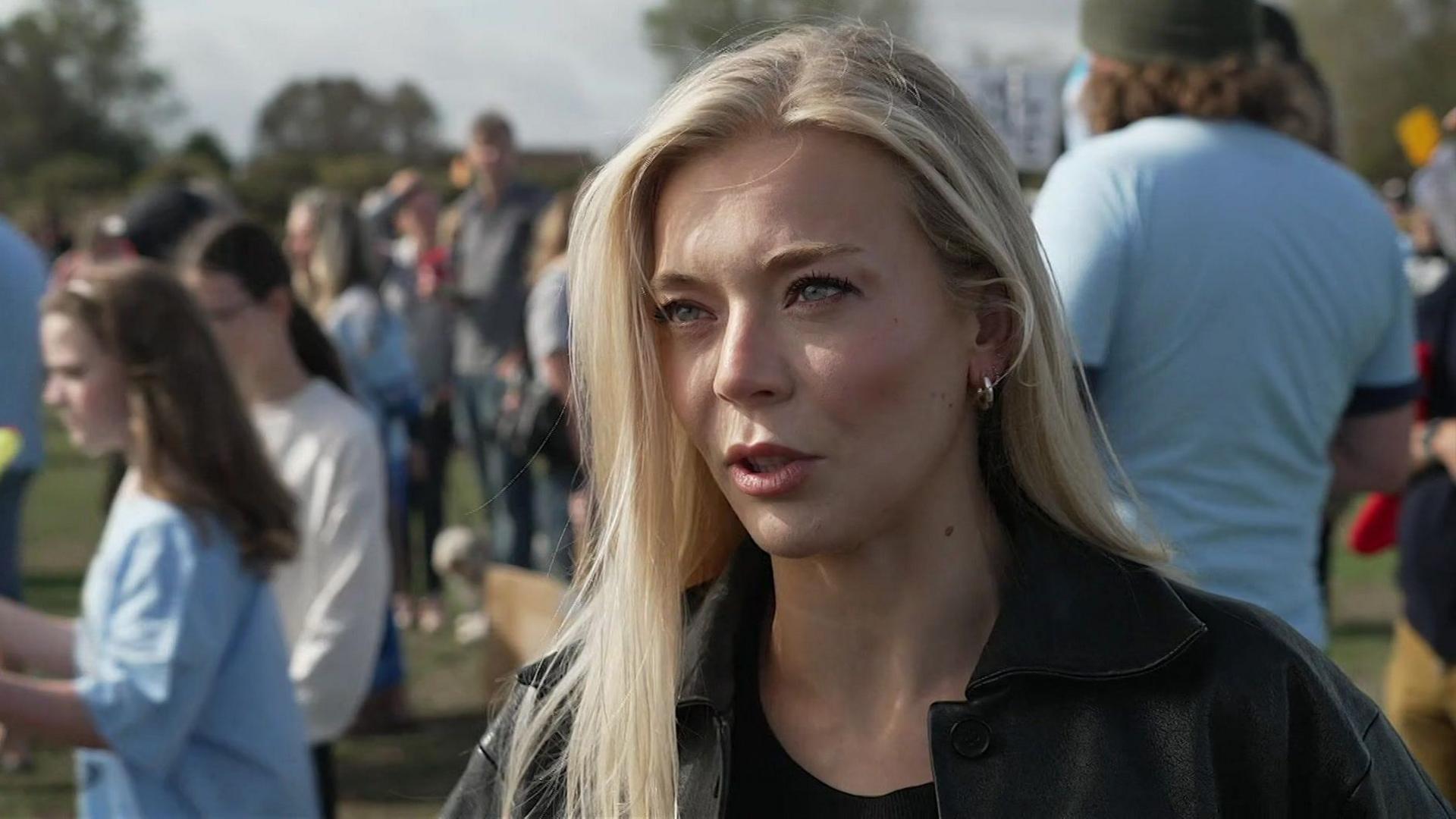 A blonde woman standing near a crowd of people at a protest.