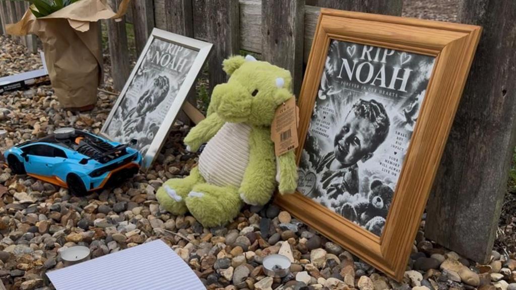 Tributes left on the ground next to a fence.