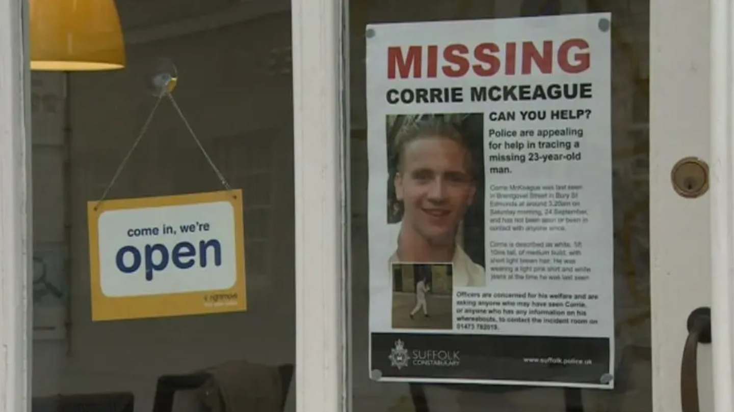 A missing persons poster which reads MISSING CORRIE MCKEAGUE in the window of a shop. On the left is a hanging sign which reads come in, we're open