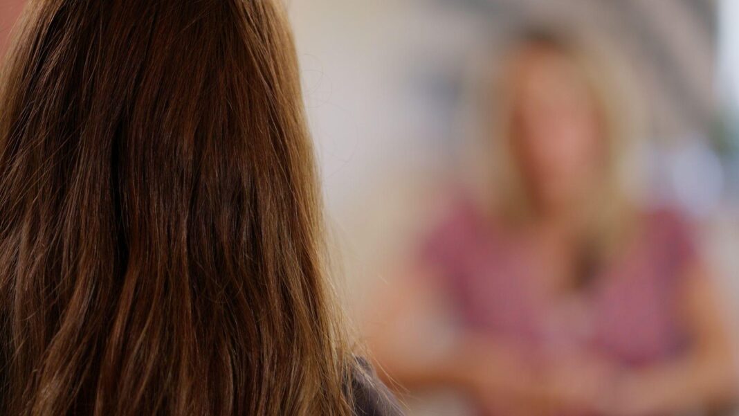 A woman with brown hair is seen from behind, talking to a woman with blonde hair and a pink top - the blonde woman is out of focus to protect her identity as she speaks to the BBC journalist