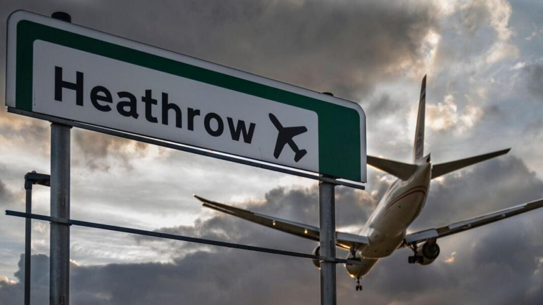 Heathrow Airport warns third runway could be delayed by four years A commercial aeroplane flying low on final approach to land at Heathrow Airport, passing directly over an overhead highway road sign.