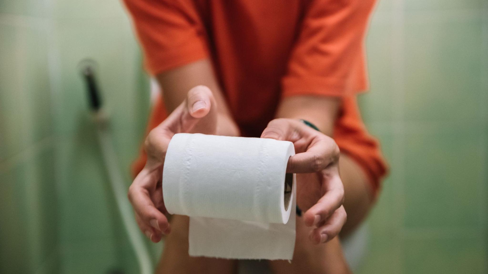 A teenage girl sits on the toilet, holding toilet paper in her hands