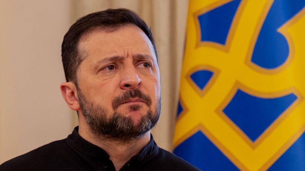 Ukraine's President Volodymyr Zelensky gives a press conference in Kyiv, standing in front of a blue and yellow flag.