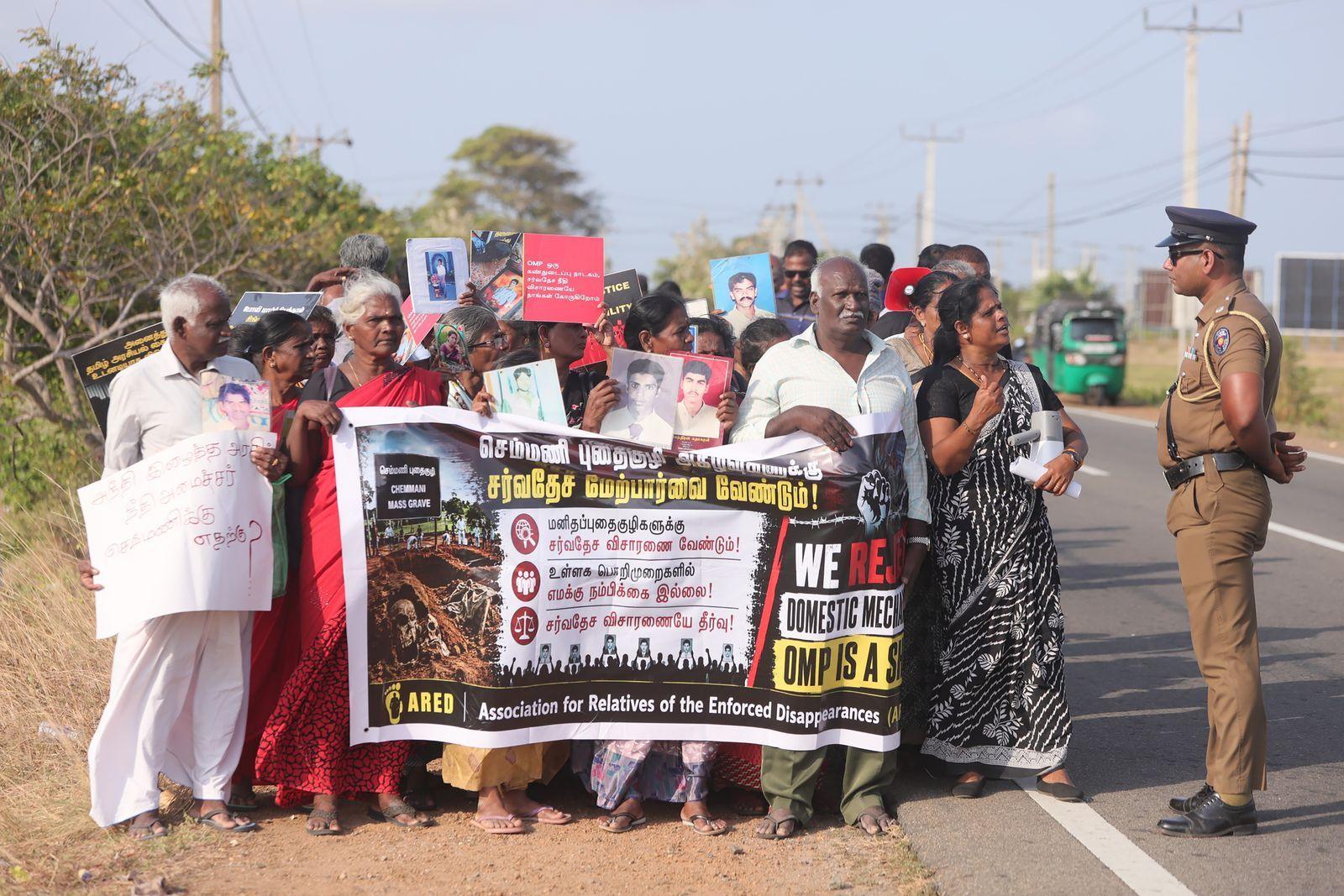 A group of people stands at a roadside behind a banner.