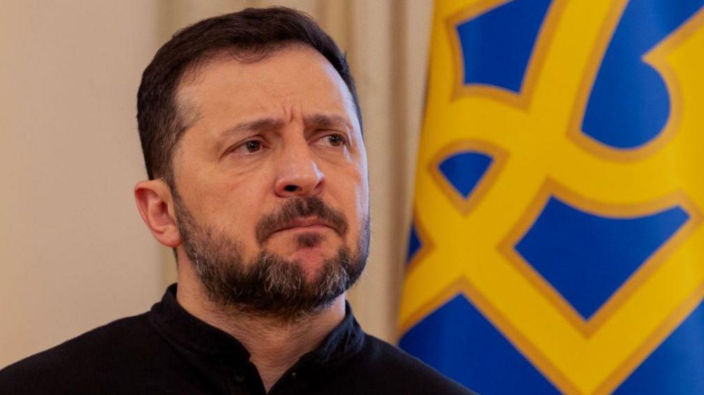Ukraine's President Volodymyr Zelensky gives a press conference in Kyiv, standing in front of a blue and yellow flag.