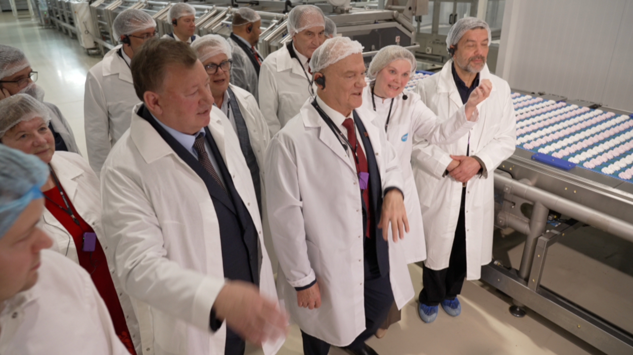 Russian Communist Party leader Gennady Zyuganov on a tour of a bread factory. He is wearing a hairnet over his bald head, and a white lab coat over a dark suit. He also has on a red tie.