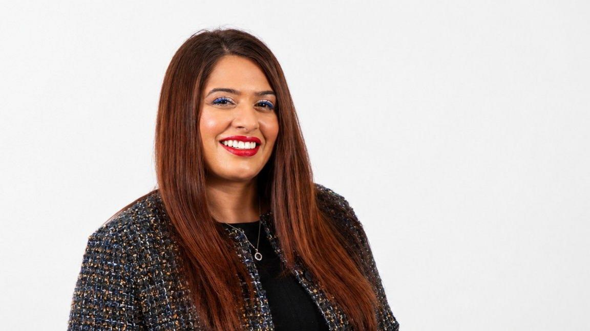 With long brown hair, Tina Chander smiles and looks into the camera.