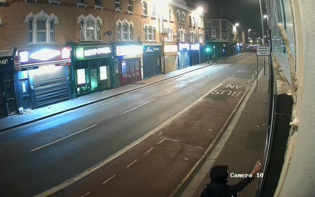 A CCTV image of a hooded figure spraying graffiti