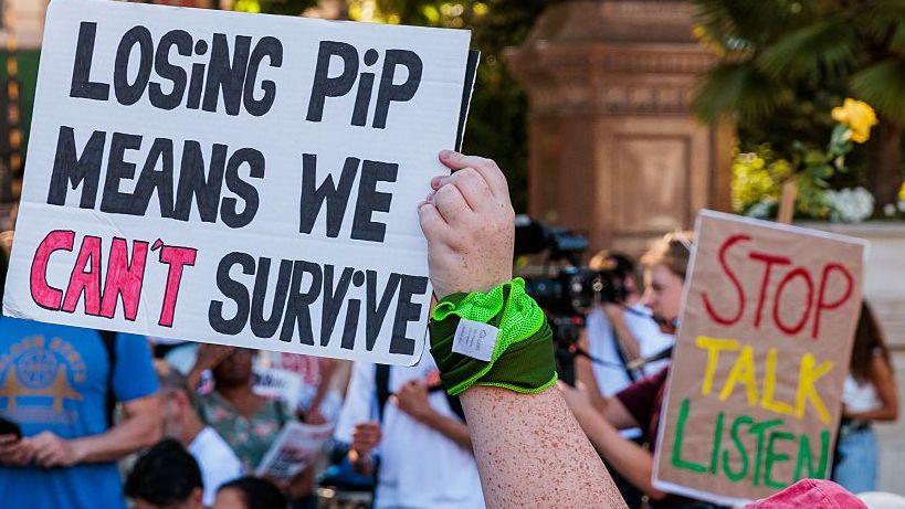 Protesters holding colourful picket signs during the stop disability benefit cuts rally in Parliament Square in 2025.