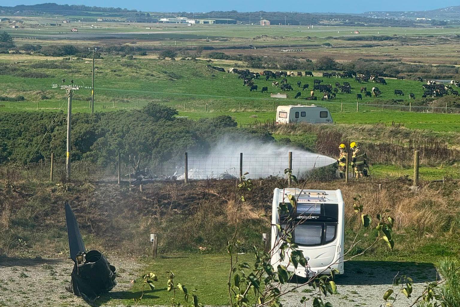 Wreckage of RAF T2 on the ground, two emergency response officers spray the wreckage with water.