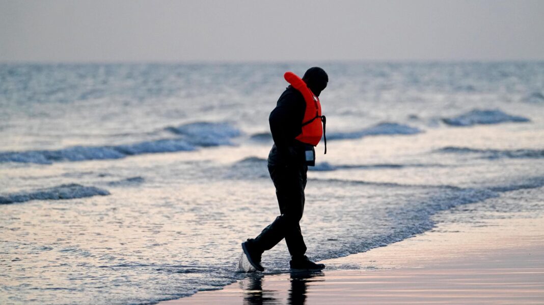 ‘One in, one out’ scheme costs £56,000 per person returned to France, home secretary says A man wearing a life jacket walks on a beach at the water's edge