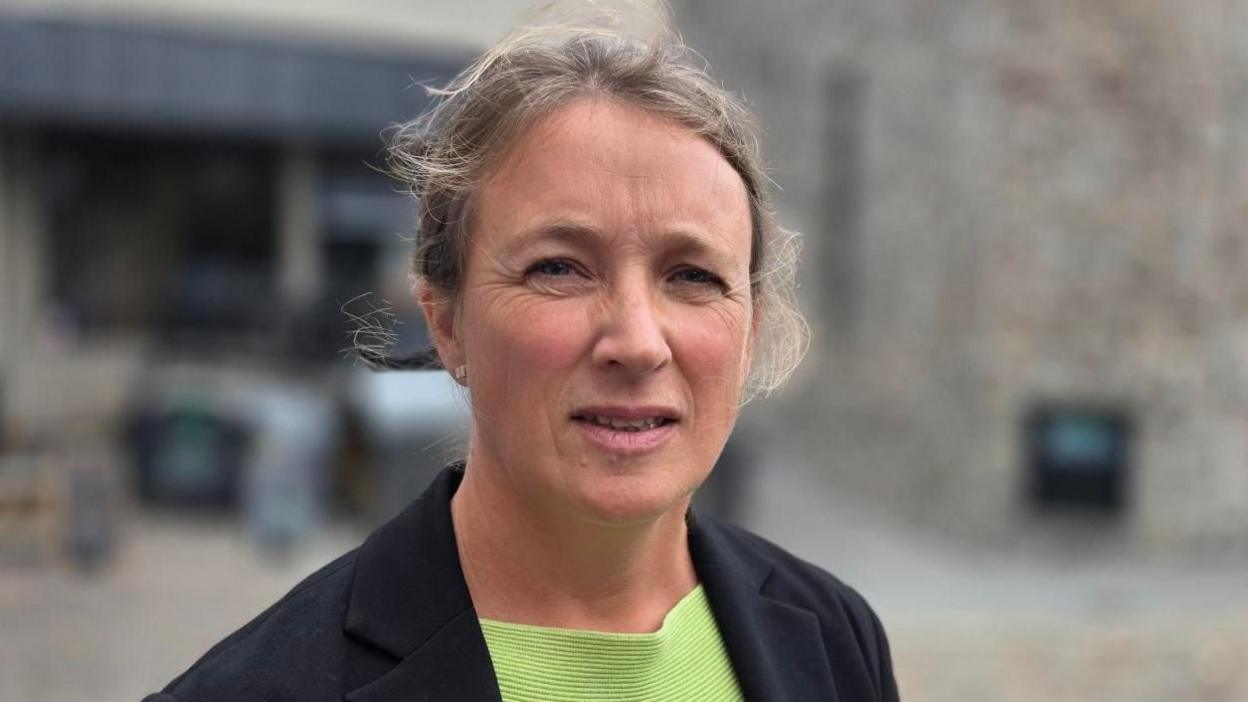 Clarissa Newell. She is wearing a green shirt and a black blazer.