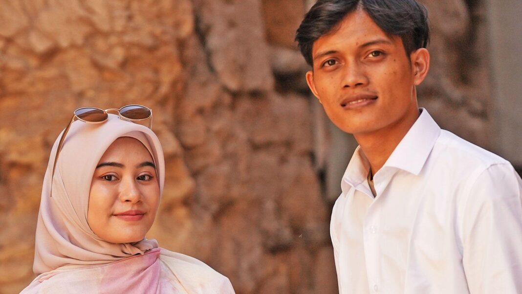 Our head teacher was an abuser. We joined forces to get justice – now we’re married Zia and Yusron smile at the camera - Zia is wearing a dusky pink hijab and has sunglasses on her head, Yusron is wearing an open neck white shirt