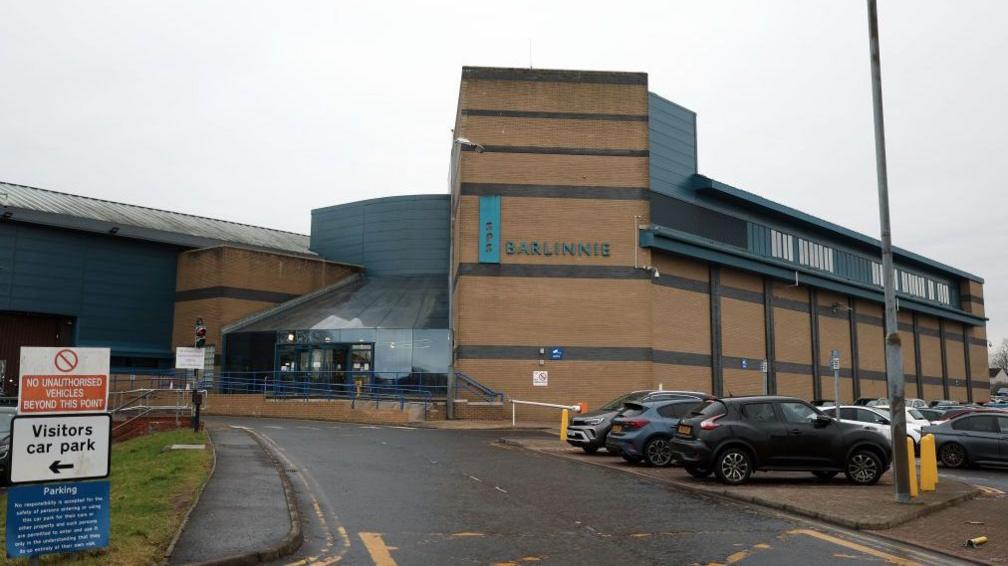 The front entrance to a prison with a Barlinnie sign and cars parked outside
