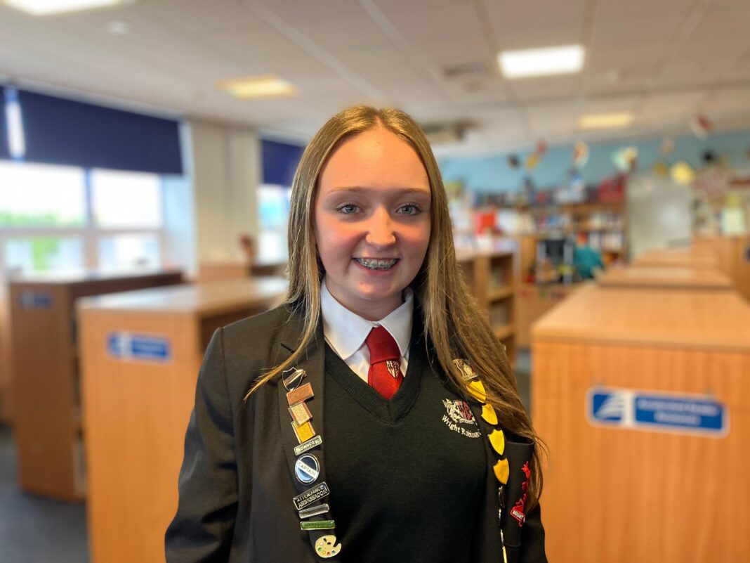 Teenagers to be offered new vocational GCSE subjects in school A blonde teenager in school uniform is smiling at the camera in the middle of the school library