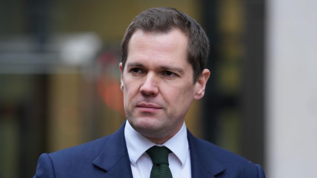 Robert Jenrick is wearing a blue suit jacket, white shirt and green tie.
