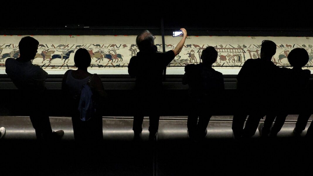 Visitors view an illuminated Bayeux Tapestry as it is displayed in a darkened exhibition room at the British Museum in London.