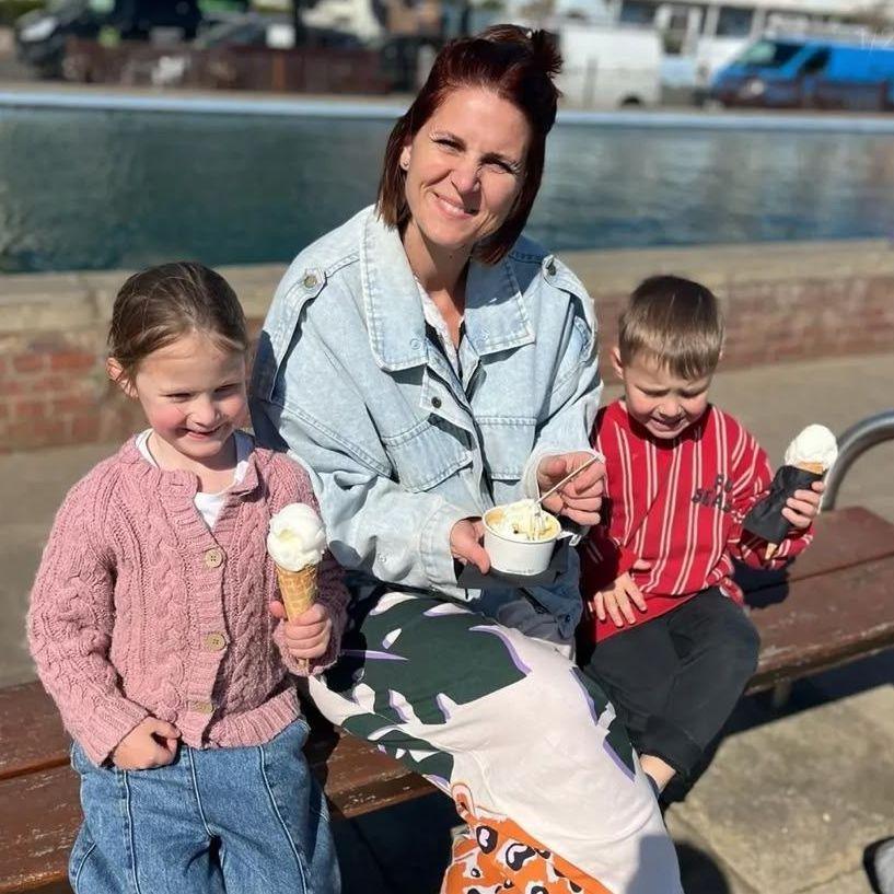 Woman and her two children sitting on a bench in the sunshine eating ice cream