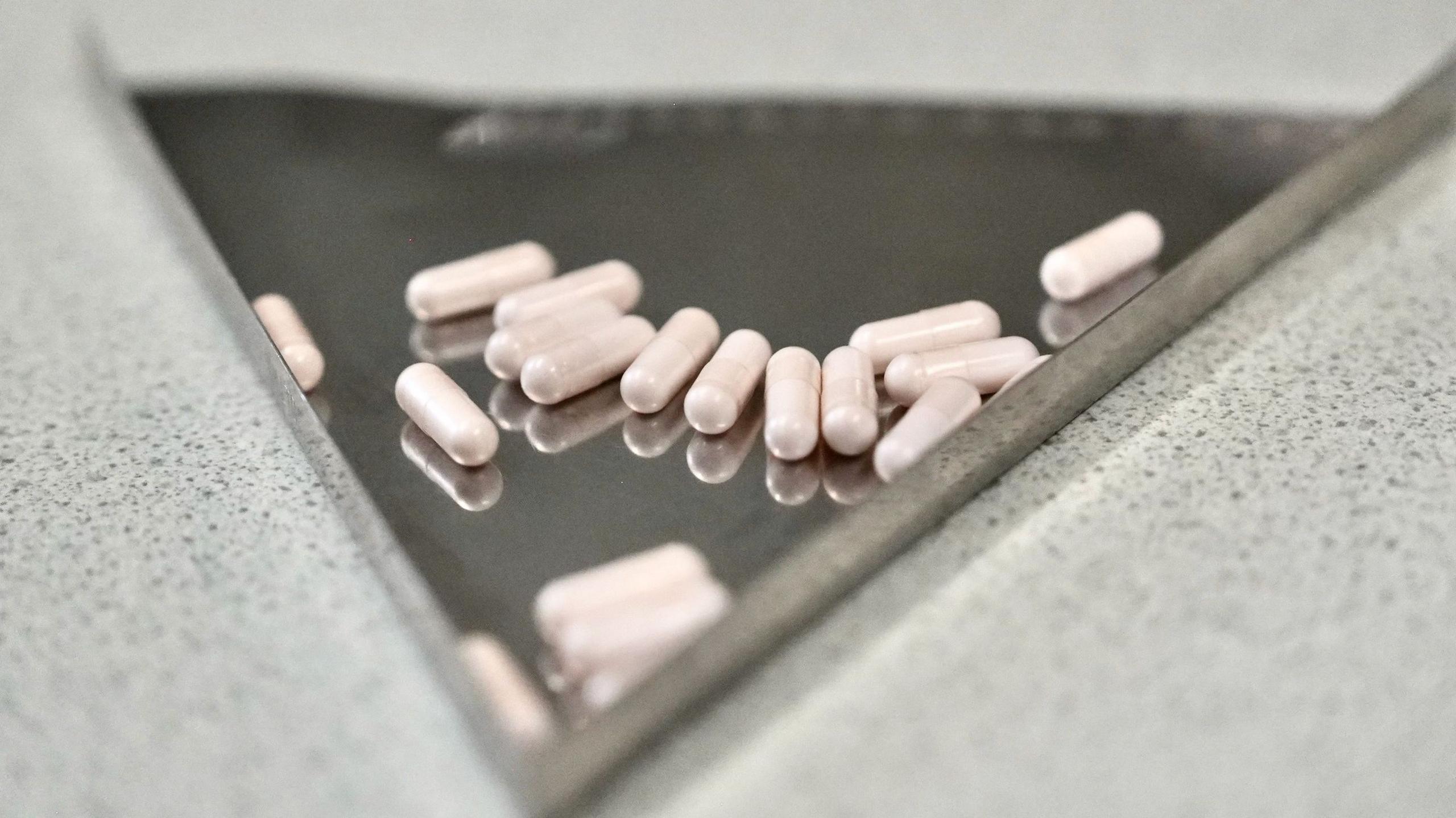 A metal medical plate with a handful of plain tablet capsules on it.