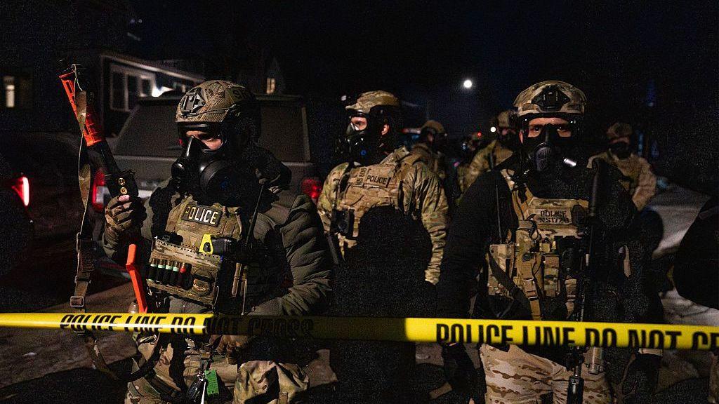US immigration officers stand behind a yellow police line in Minnesota at night after protesters clashed with ICE agents in north Minneapolis in January 2026.