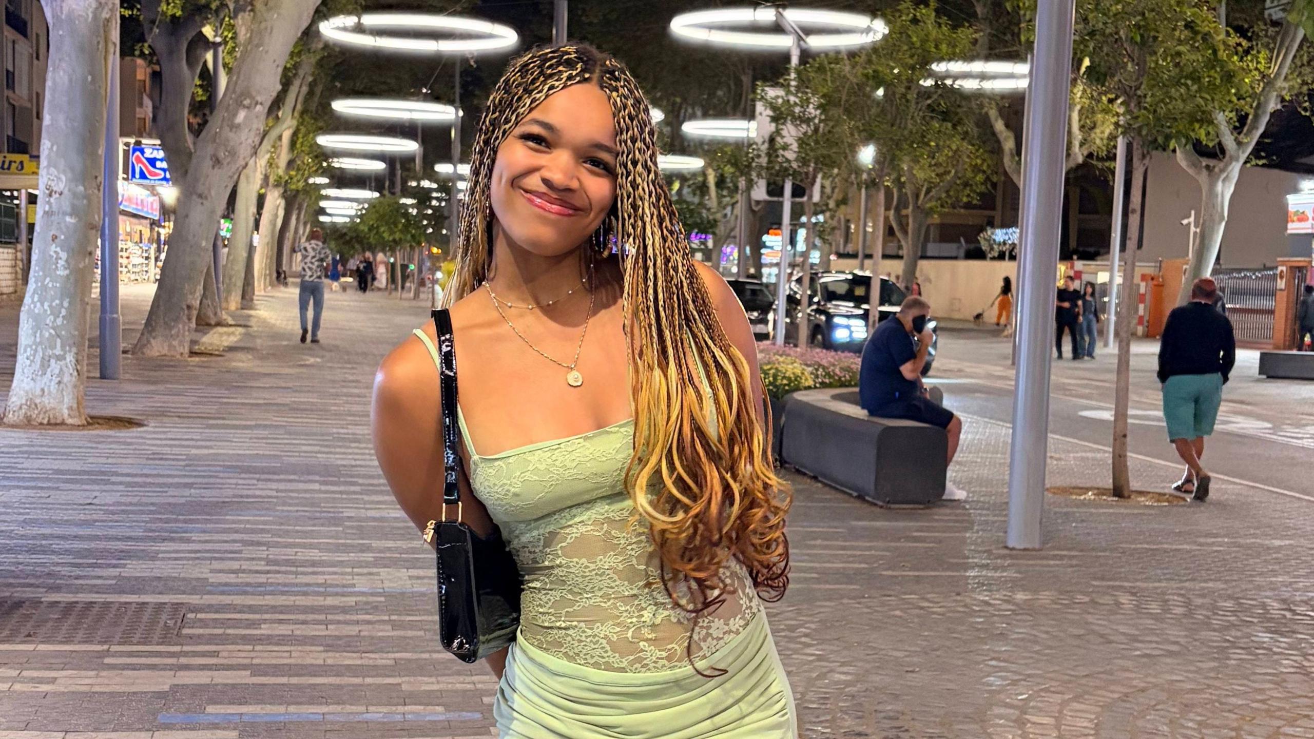 Jayda is standing facing the camera. She is wearing a green dress and is smiling at the camera. She is standing on a street at night