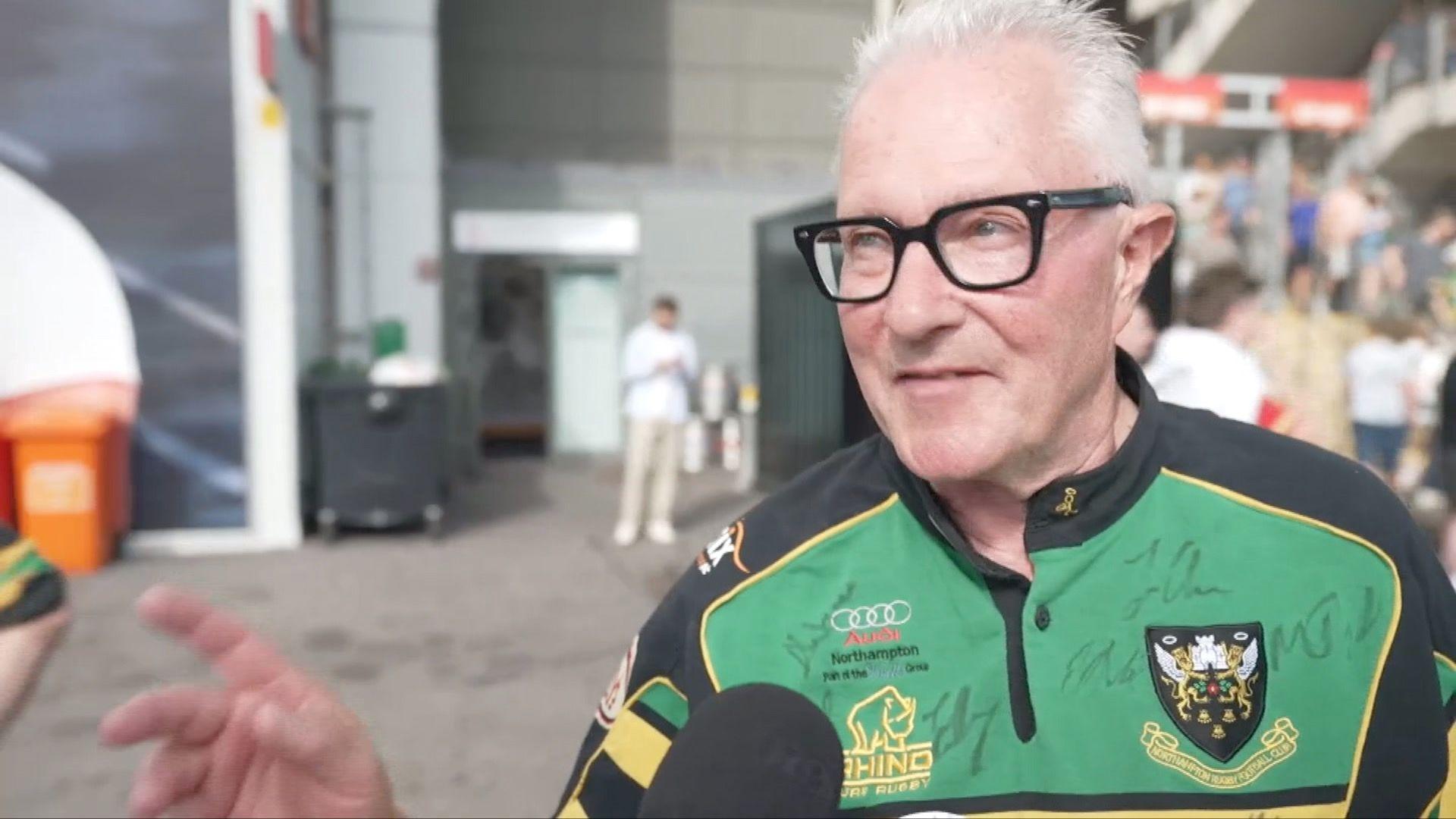 An older fan dressed in the green Saints kit, covered in autographs, is speaking to somebody off camera
