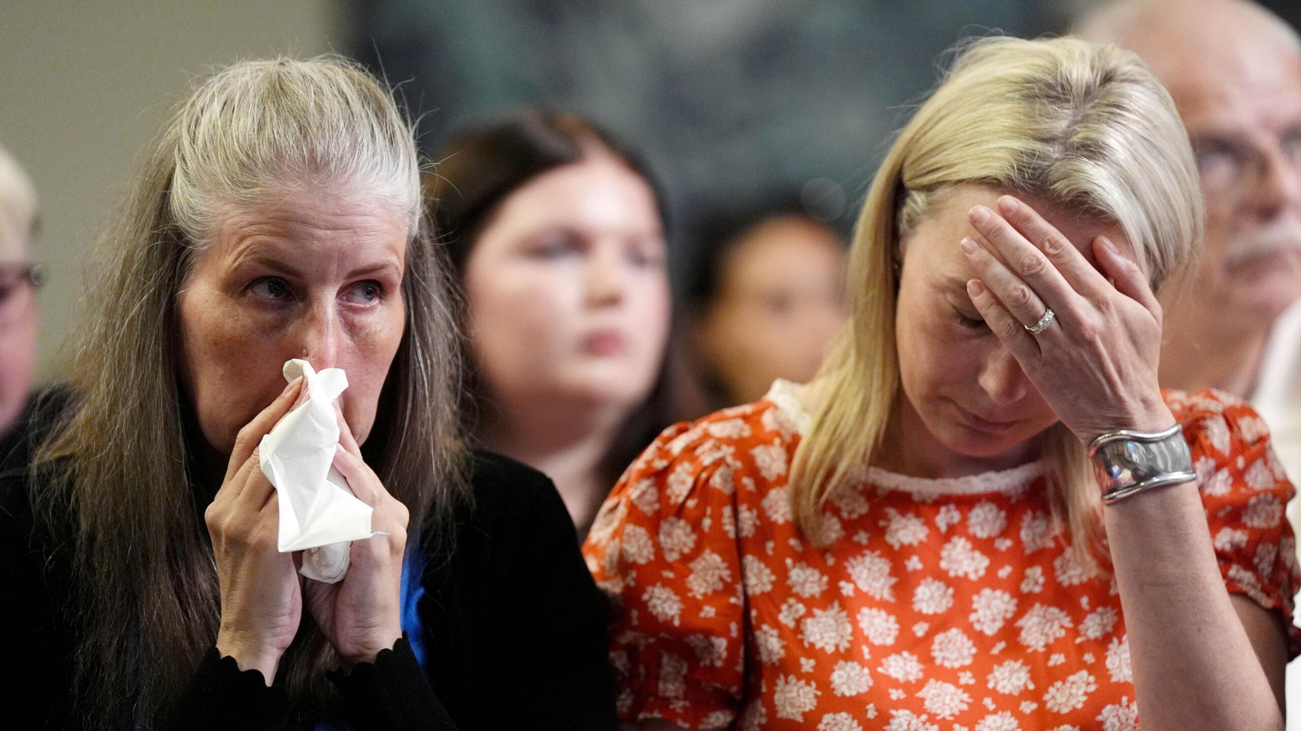 Sarah Hawkins holds a tissue to her face and appears tearful. Sarah Hawkins, sitting next to her, holds her hand to her forehead.