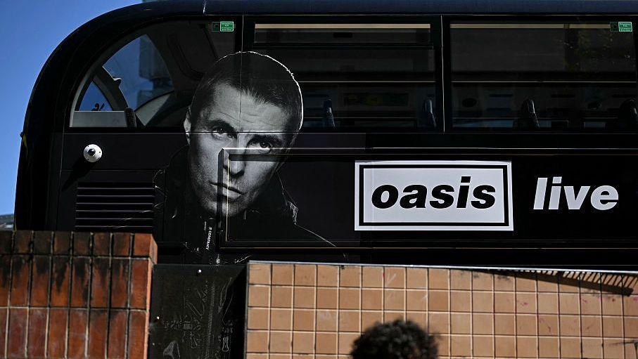 A large black bus with the words "OASIS LIVE" written on the side and a photo of Liam Gallagher