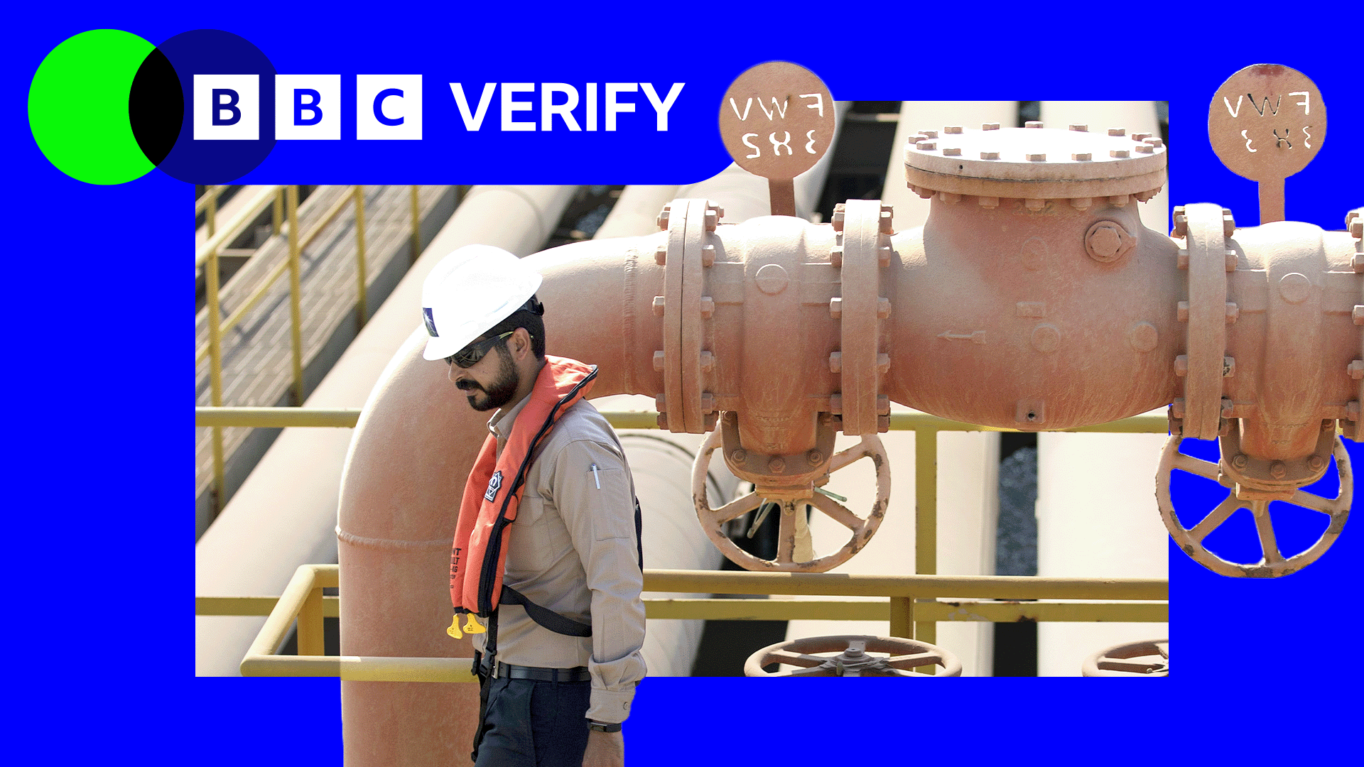 A oil industry worker in Saudi Arabia wearing a protective helmet walks next to a pipe with several valves