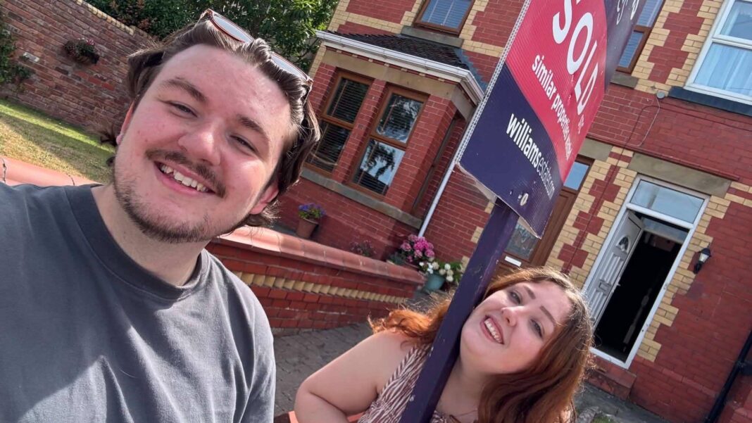 Why we bought our first home with a 100% mortgage – despite the risks Bronya and George are standing in front of a 'sold' sign outside their red-brick terraced home. They are both smiling at the camera.