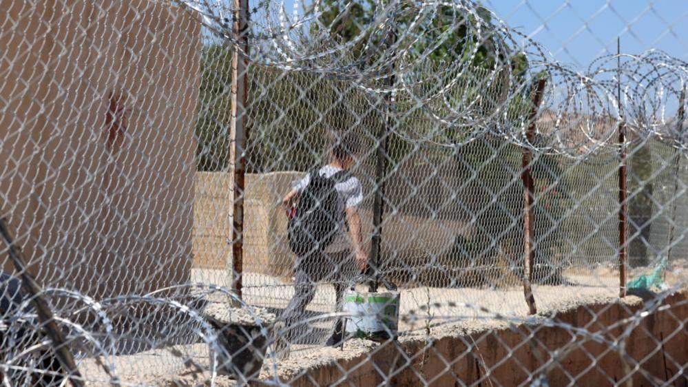 A Palestinian boy, seen through a security fence bordering the school campus, leaves on the first day of the new academic year, in the village of al-Mughayyir, near Ramallah, West Bank. Photo: 6 September 2026