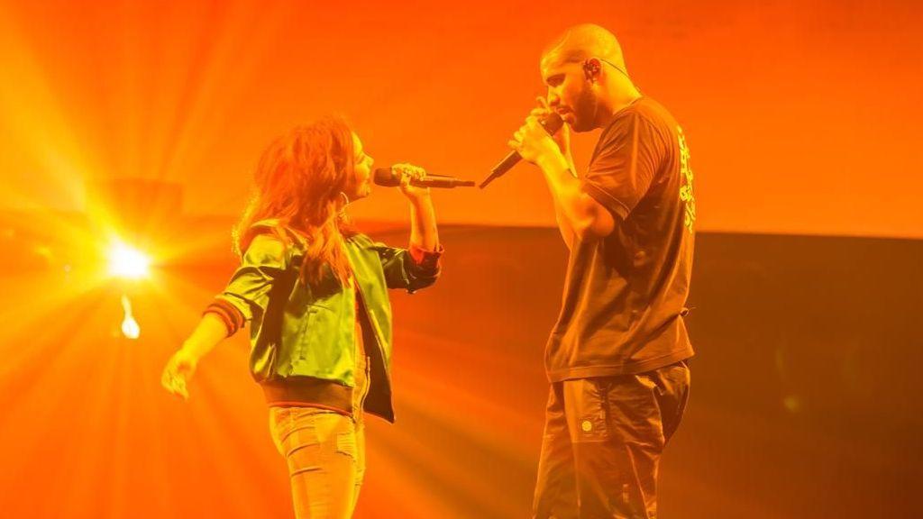 Kyla performs with Drake on stage. An orange hue is cast over them.