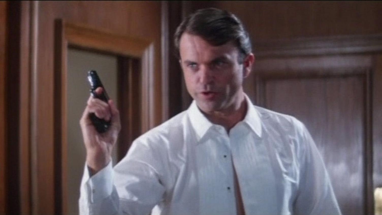 Sam Neill in a white shirt and holding a gun as part of his audition for Bond