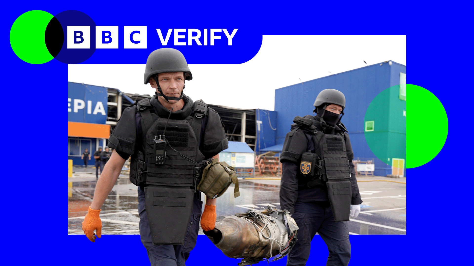 Two Ukrainian first responders carry the remains of a Russian jet-powered drone engine after an attack. They are wearing body armour and helmets and are holding opposite ends of the engine.