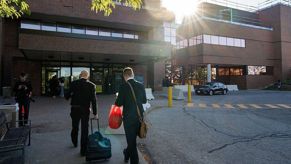 Two men are seen outside a court building wheeling small cases into the office