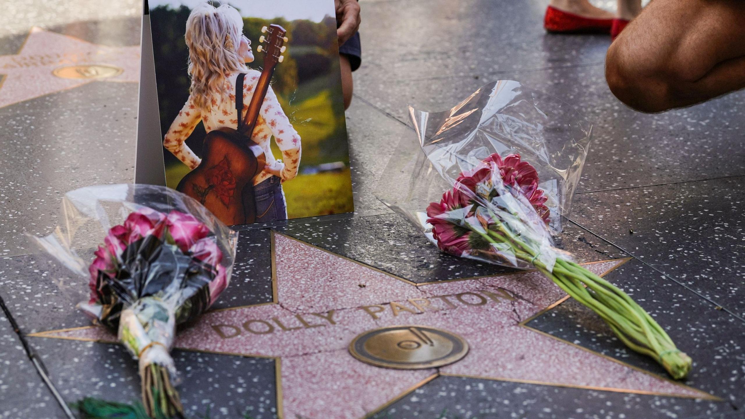 A star on the pavement with Dolly Parton's name, and two bunches of red flowers and a photo laid on it