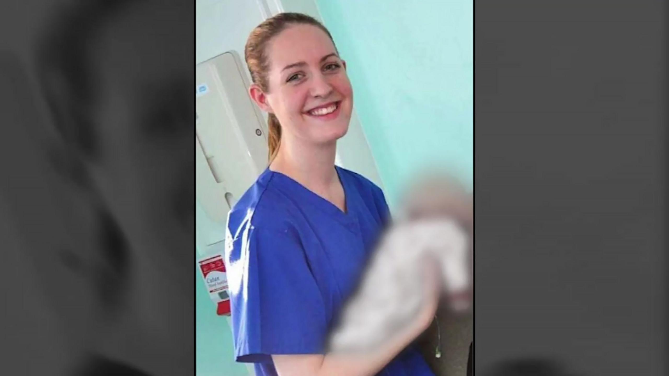 Lucy Letby in scrubs holding a baby (blurred out) and smiling at the camera