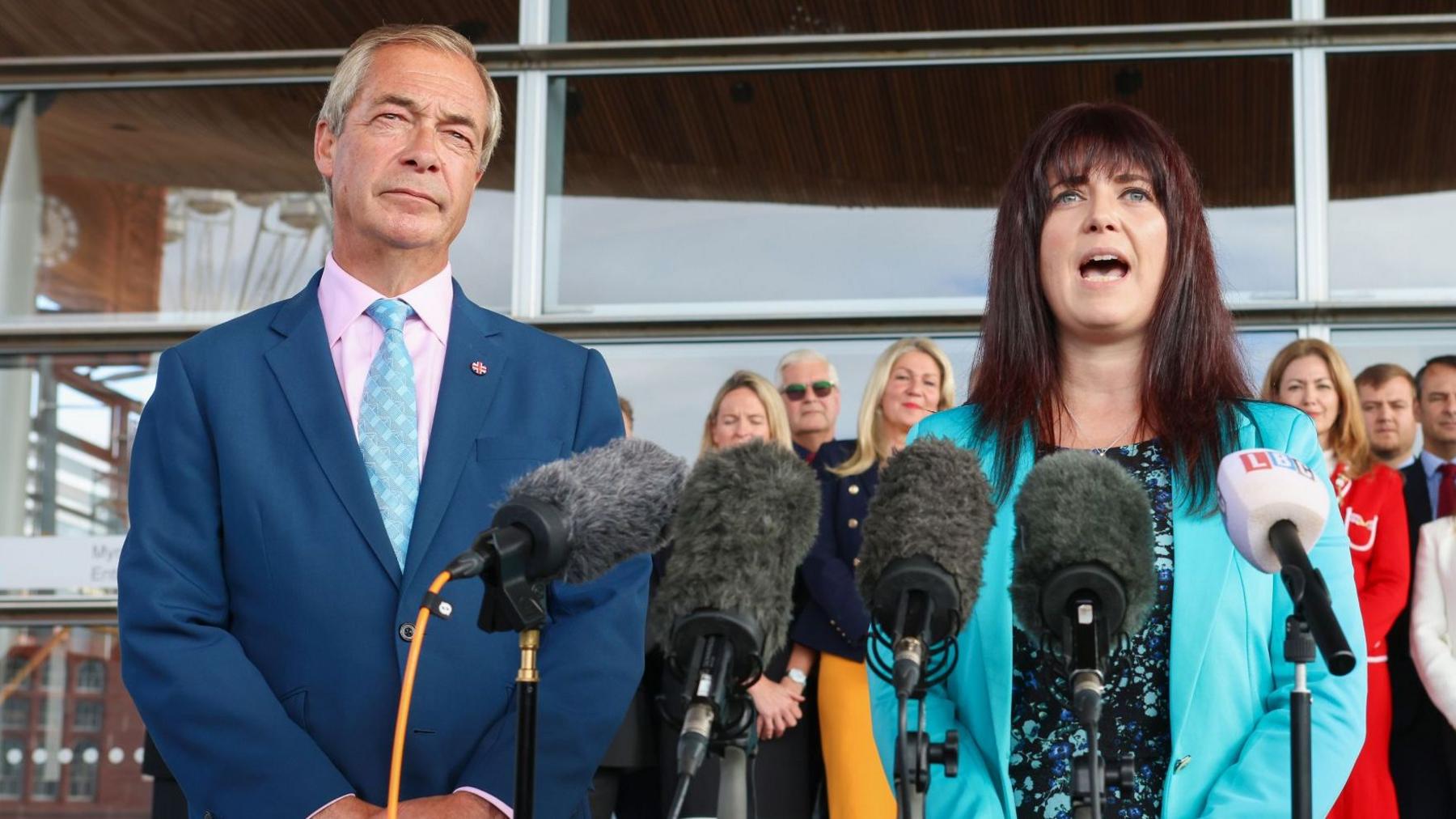 Nigel Farage and Helen Jenner speak into a row of microphones as part of a press conference.