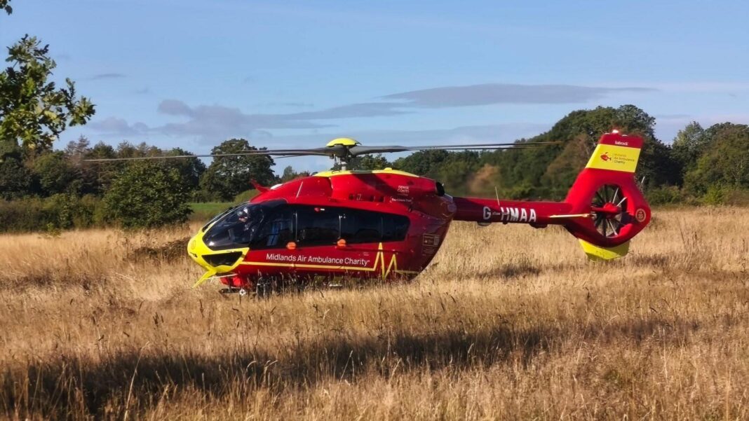 Police probe after child dies in woodland A midlands air ambulance which is red and has a yellow nose, tail and roof. it is parked in a field of brown grass